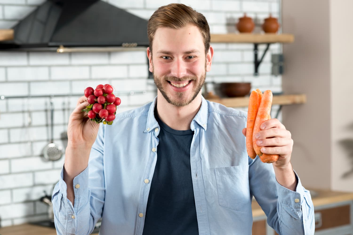 Man holding radishes and carrots in kitchen.